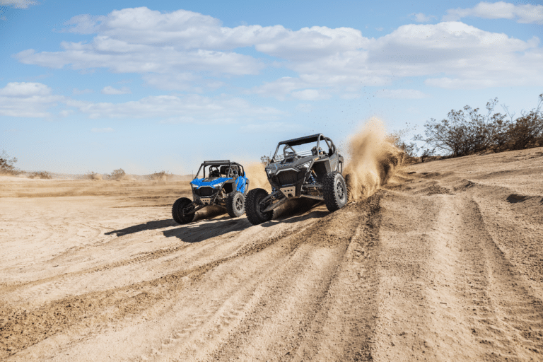 Two Polaris RZR side-by-sides riding a sandy desert trail